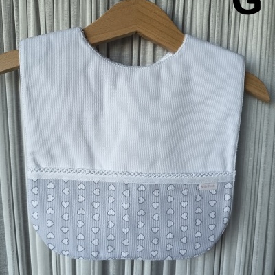 Babete de bebé branco e cinzento com padrão de corações pendurado num cabide de madeira.