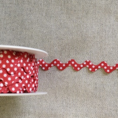 Carretel de fita vermelha com pintas brancas em padrão zigzag sobre tecido cinzento