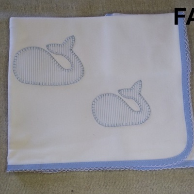 Fralda branca com bordas azuis e bordados de baleias azuis sobre tecido bege