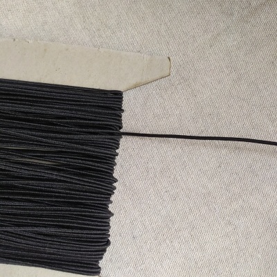 Fio elástico preto enrolado num cartão branco sobre tecido bege claro