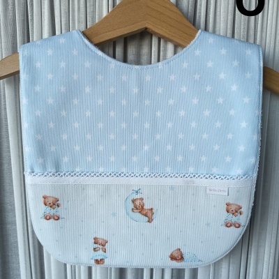 Babete azul claro com estrelas brancas e desenhos de ursinhos, pendurado em cabide de madeira