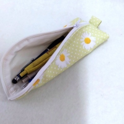 Estojo de tecido amarelo claro com padrão de margaridas e fecho branco aberto com objetos dentro