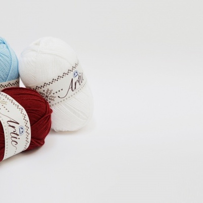 Tres novelos de lã em azul claro, branco e vermelho com rótulos brancos