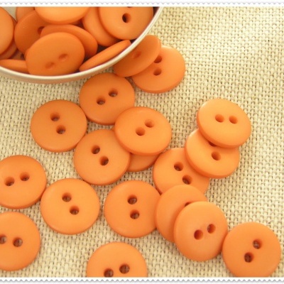 Botões laranja redondos com dois furos sobre superfície bege