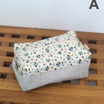 Necessaire retangular com padrão floral azul e amarelo e base cinza, fecho branco, sobre bancada de madeira