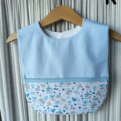 Babete azul claro com padrão de bolinhas brancas e estampado de animais de quinta em cabide