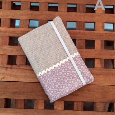 Caderno com capa de tecido bege e rosa floral com faixa elástica branca numa mesa de madeira.