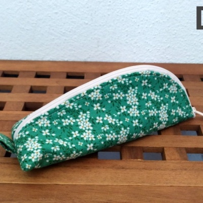 Estojo verde com flores brancas e amarelas sobre superfície de madeira