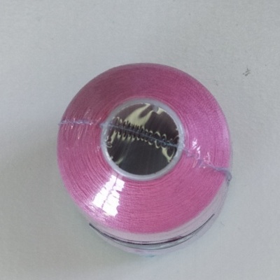 Rolo de linha cor-de-rosa embalado em plástico sobre superfície branca