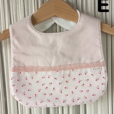 Babete de bebé cor de rosa com padrão floral pendurado num cabide de madeira