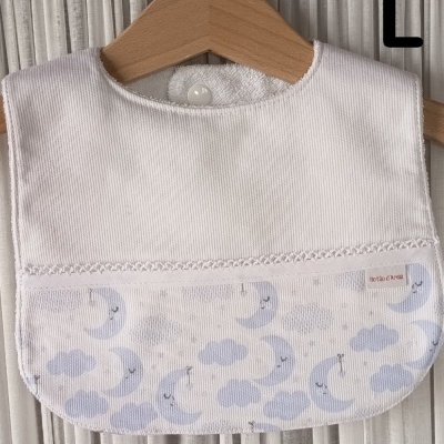 Babeiro branco com padrão de luas e nuvens azuis pendurado em cabide de madeira