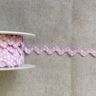 Rolo de fita rosa com pintas brancas em padrão ziguezague sobre tecido bege