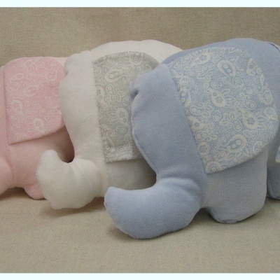 Três elefantes de peluche coloridos em rosa, branco e azul sobre fundo bege