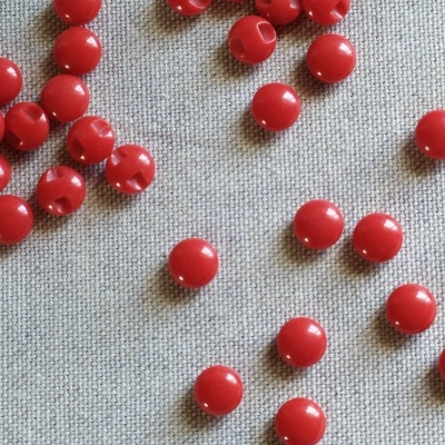 Contas vermelhas redondas sobre tecido cinza com texto 'Vermelho'