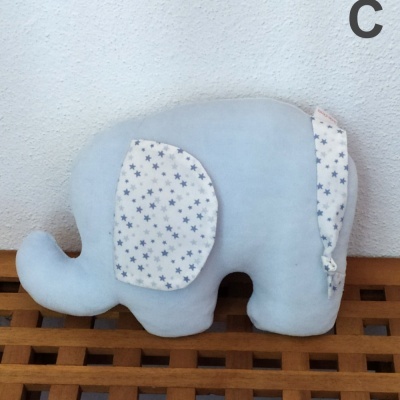 Almofada elefante azul claro com orelhas brancas com estrelas azuis sobre madeira