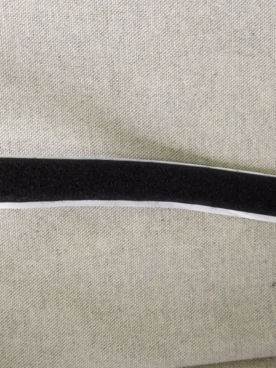 Cabide preto aveludado com contorno branco sobre tecido cinzento