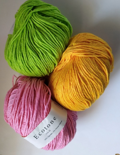 Três novelos de fio de algodão em verde, amarelo e rosa com etiqueta Ecotone