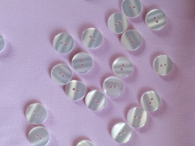 Botões brancos redondos com dois furos sobre tecido rosa claro