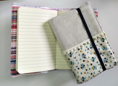 Dois cadernos, um aberto com capa listrada e outro fechado com capa floral e elástico preto