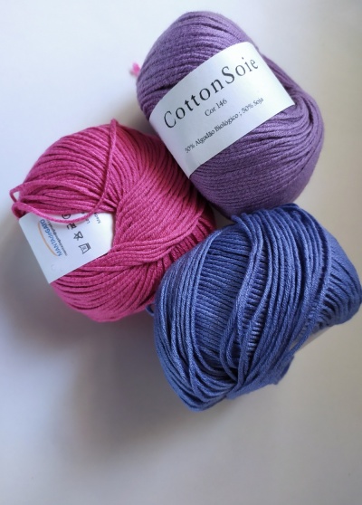 Novelos de lã lilás, rosa e azul com rótulo em fundo branco