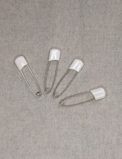 Alfinetes de segurança com cabeça branca sobre tecido cinzento