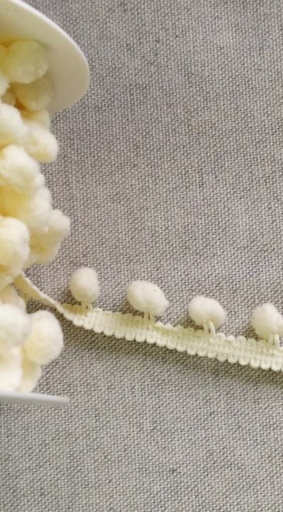 Fita de pompons brancos felpudos sobre tecido cinza.