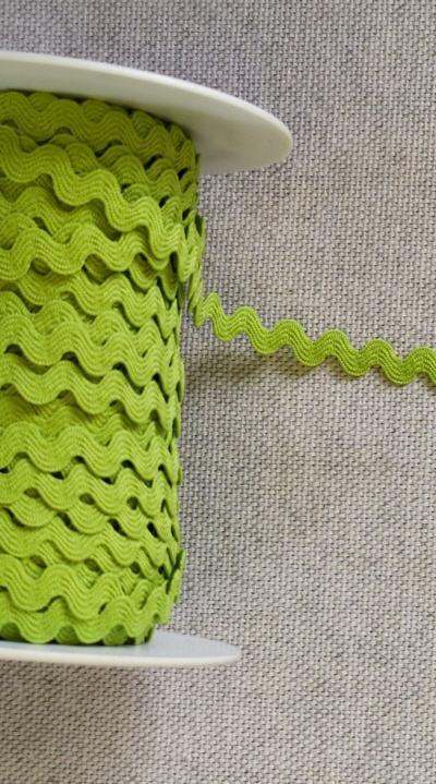 Rolo de fita zig-zag verde fluorescente num carretel branco sobre tecido cinzento