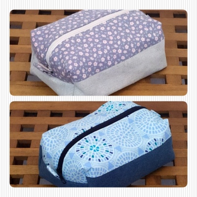 Duas bolsas de tecido com fecho, padrões diferentes, sobre mesa de madeira.