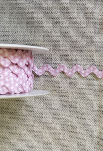 Fita ziguezague rosa com bolinhas brancas sobre tecido cinza
