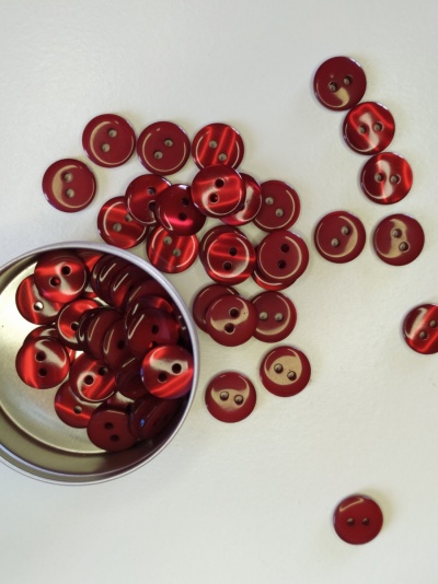 Botões vermelhos de dois furos em superfície branca com caixa metálica aberta