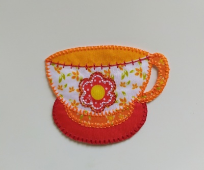Aplicação em tecido em forma de chávena de chá colorida com flor central.