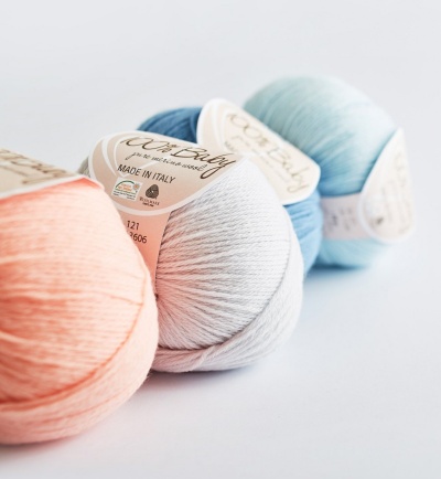 Quatro novelos de fio de algodão em tons pastel com etiquetas sobre fundo branco