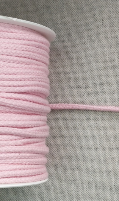 Carretel de fio de algodão rosa claro trançado sobre tecido cinza