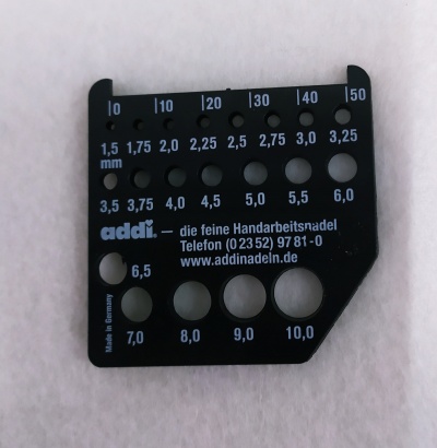 Mostrador de plástico preto para medir agulhas com furos de vários diâmetros e texto impresso.