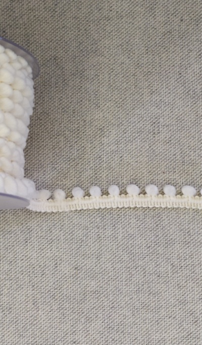 Fita decorativa branca com bolas em carretel sobre tecido cinzento