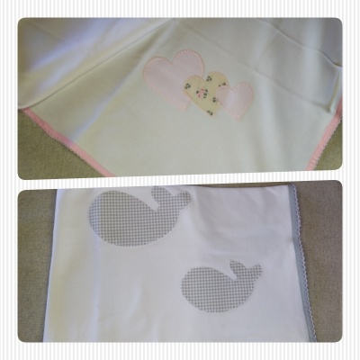 Dois panos de tecido branco com aplicações decorativas, corações e baleias