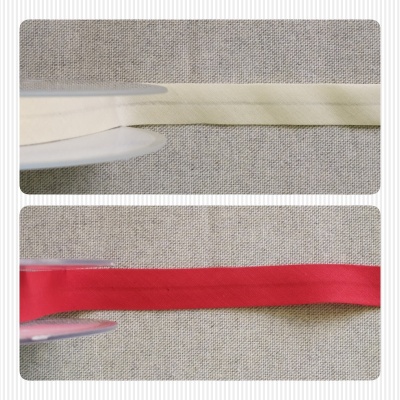 Duas fitas de tecido, branca e vermelha, sobre fundo de tecido cinzento, com faca branca ao lado.