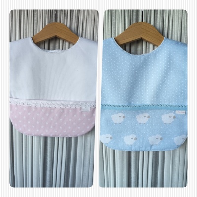 Dois babetes para bebé rosa e azul pendurados em cabides de madeira