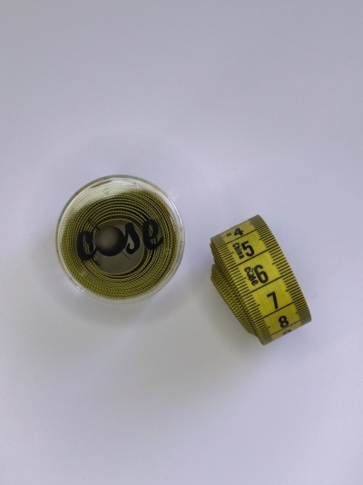 Fita métrica amarela enrolada dentro de recipiente transparente sobre fundo branco