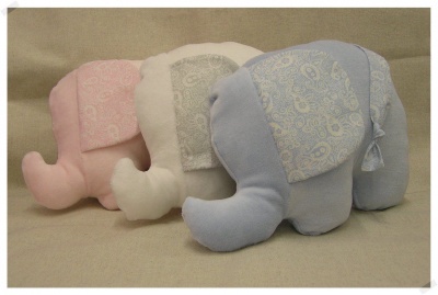Três peluches de elefante em rosa, branco e azul com padrão floral nas orelhas