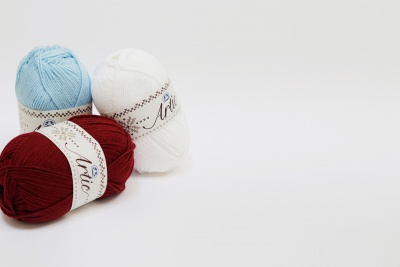 Tres novelos de lã em azul claro, branco e vermelho com rótulos brancos