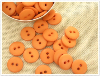 Botões laranja redondos com dois furos sobre superfície bege