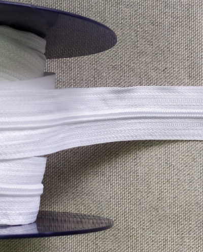 Rolo de elástico branco sobre disco azul numa superfície de tecido cinza