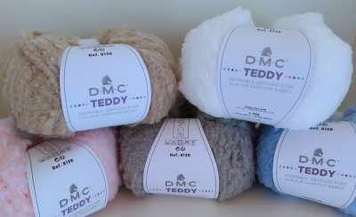 Cinco novelos de lã DMC TEDDY em cores bege, branco, rosa, cinzento e azul com etiquetas brancas.