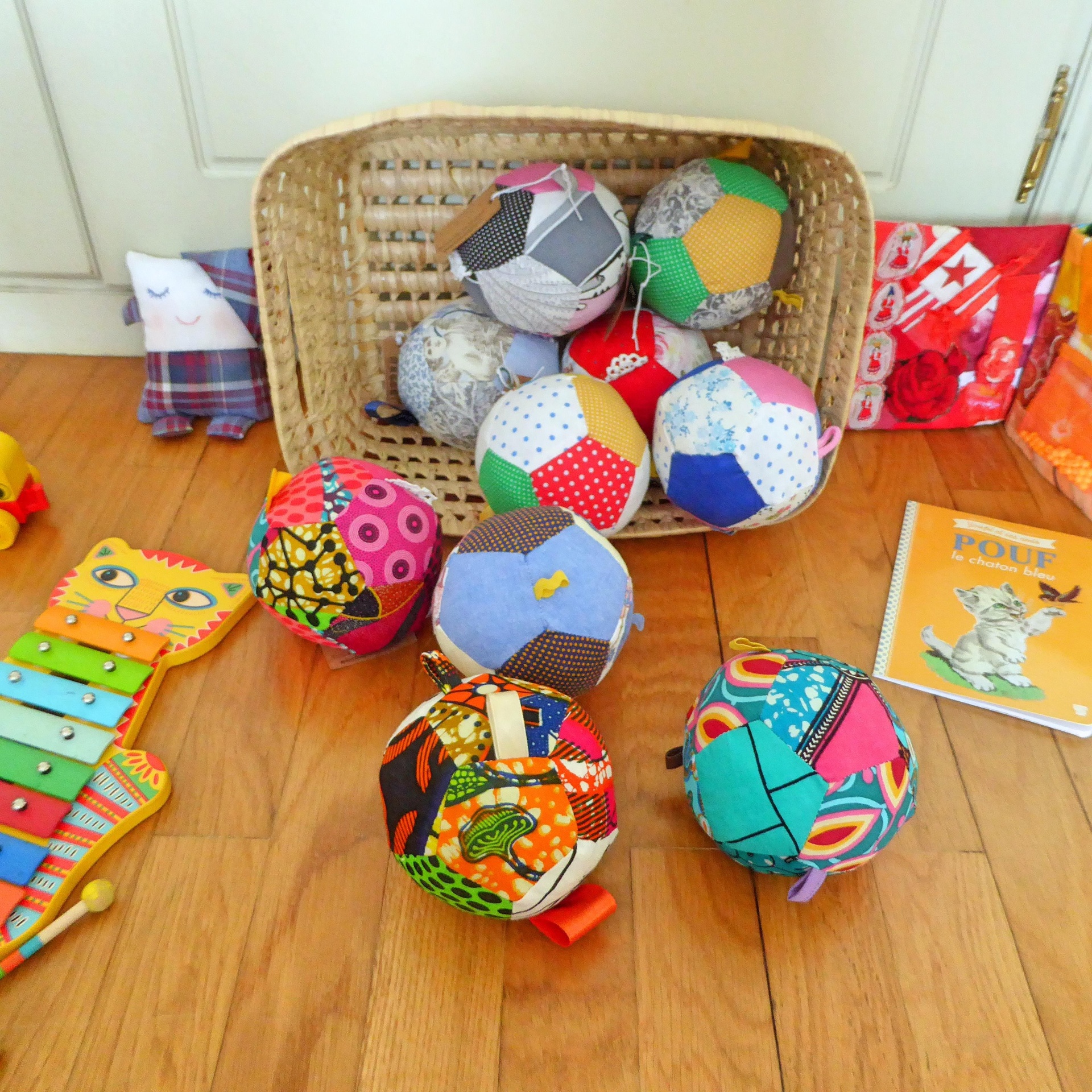 Kuka - Bola suave para bebé, em tecido Bolas de retalhos coloridos num cesto e chão de madeira com brinquedo xilofone amarelo e livros infantis