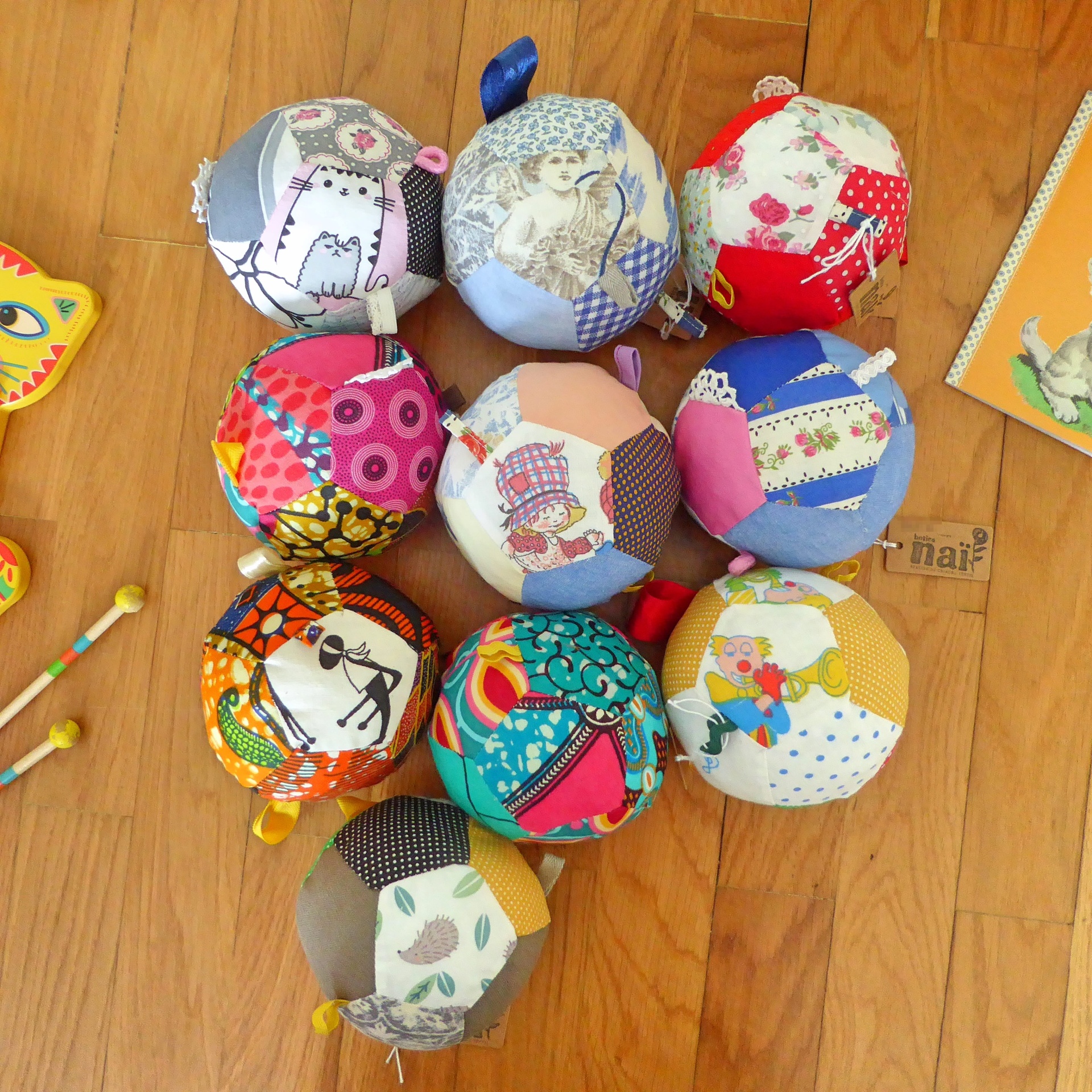 Kuka - Bola suave para bebé, em tecido Bolas de patchwork coloridas com diferentes estampas sobre chão de madeira
