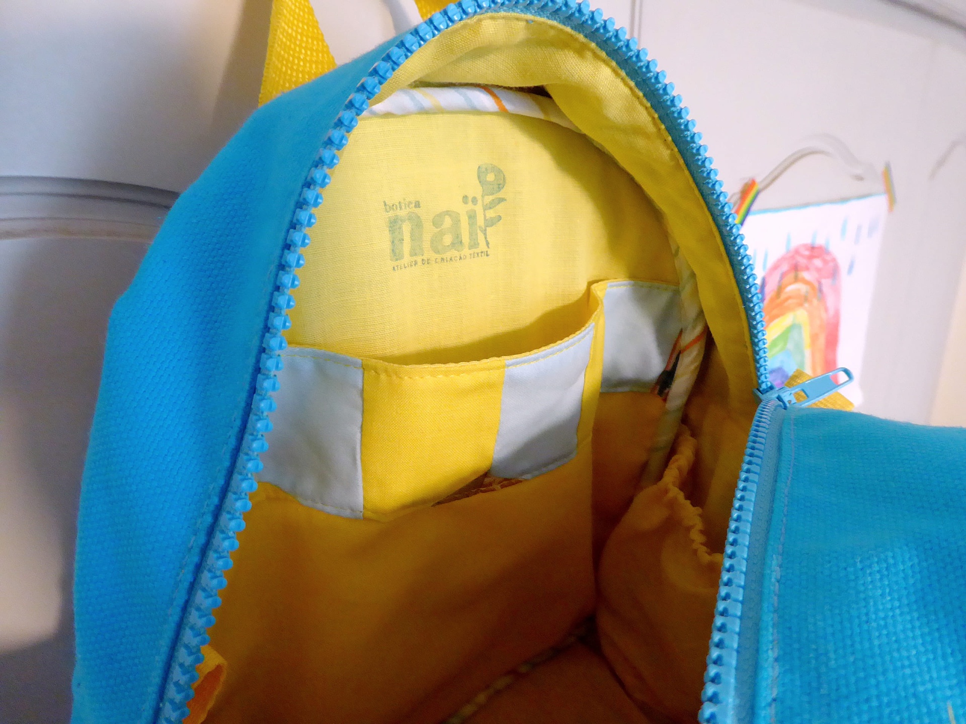 Mochila Pequena Interior de mochila azul e amarela com etiqueta na parte interna