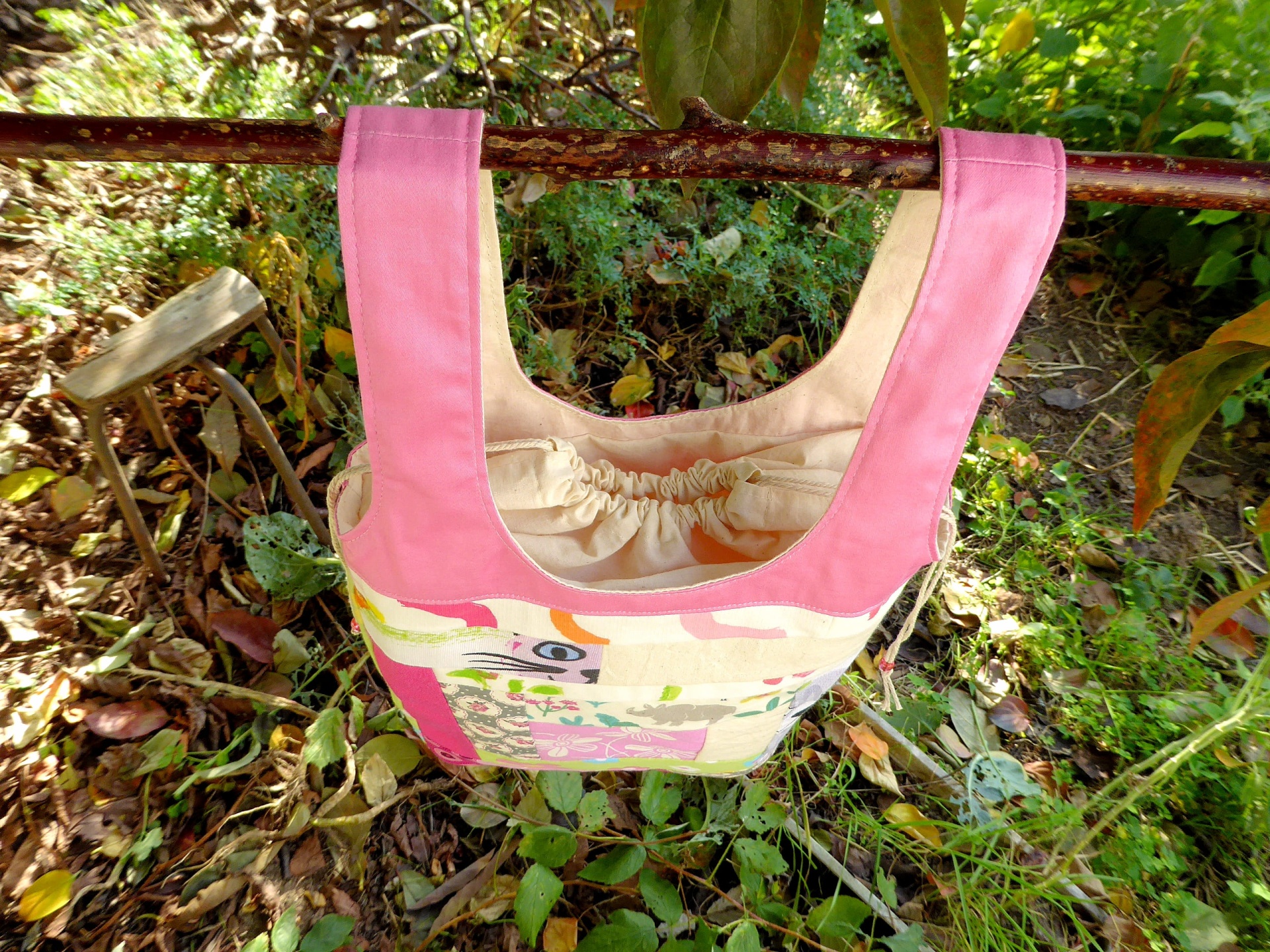 Sacos Com Asas / Saco do Pão Mala de tecido cor de rosa e bege com padrão colorido pendurada num ramo em ambiente natural