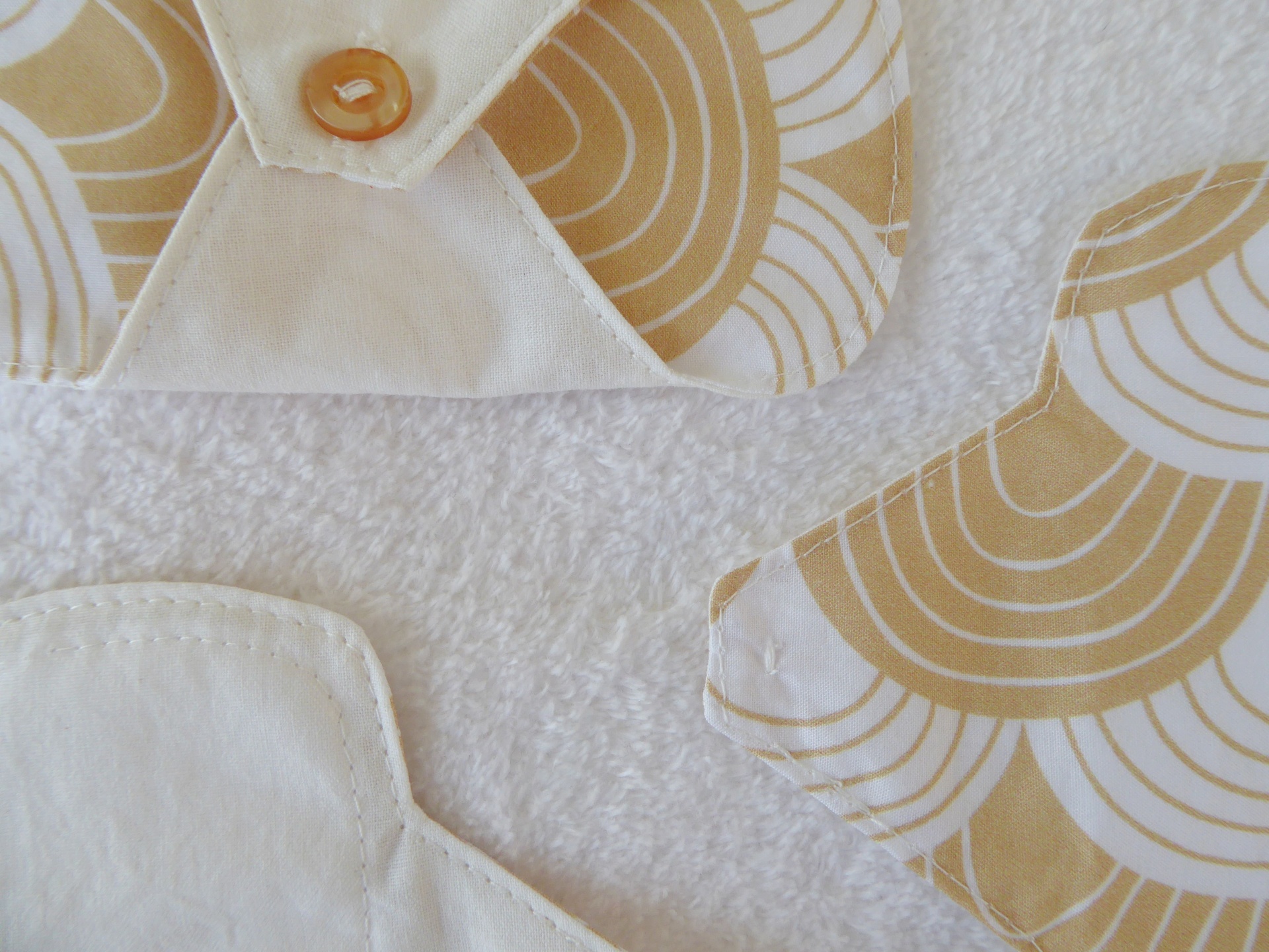 Pensos Diários Mini 13cm Têxtil branco com padrão bege creme e botão castanho sobre fundo branco felpudo