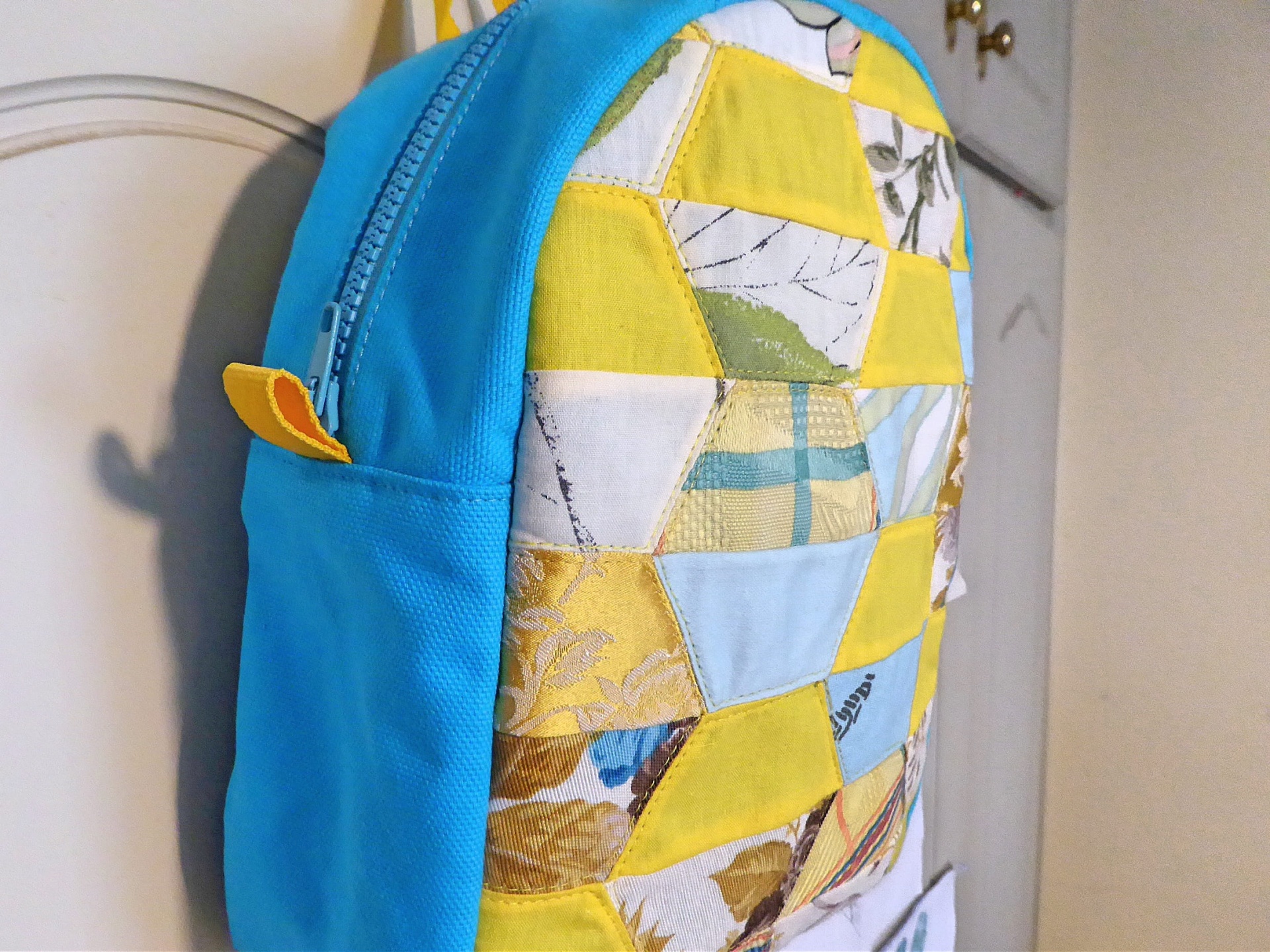 Mochila Pequena Mochila azul com patchwork amarelo e azul pendurada numa porta